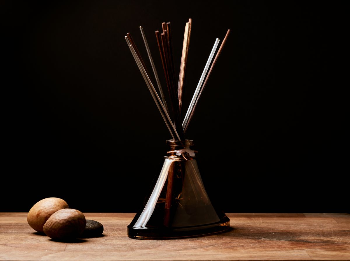 Close-up of a wood incense stick resting against a glass bottle